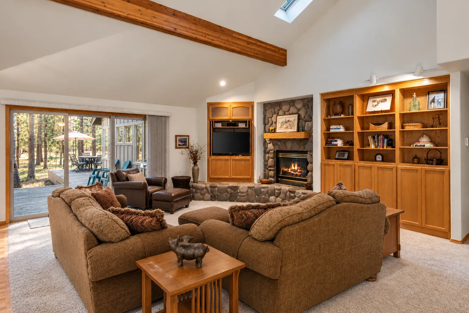 Vaulted great room with beamed ceiling, river-rock gas fireplace, built-in shelves and sliding doors to the deck